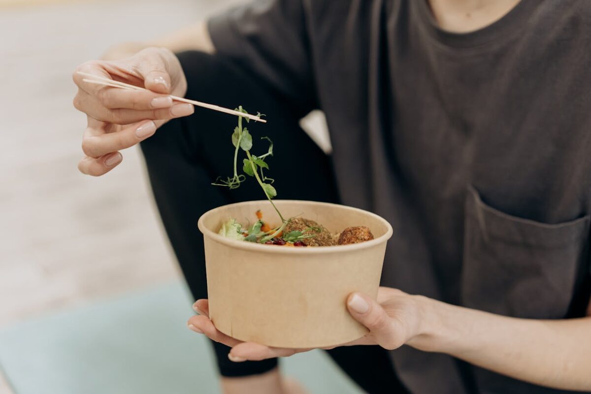 services-01 A woman holding a paper bowl filled with a healthy vegetarian meal in an indoor setting, promoting wellness.